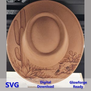 May include: A tan hat with a desert scene design. The hat has an engraved image of a saguaro cactus, desert plants, and a skull. The text "SVG", "Digital Download", and "Glowforge Ready" are visible on the hat.
