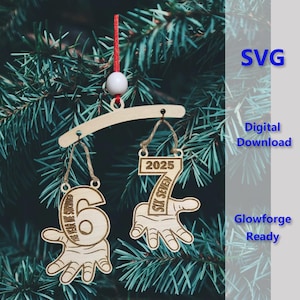 Puede incluir: Adorno navideño de madera con los números 6 y 7, cada uno sostenido por una mano. El número 6 dice "THE YEAR WE SURVIVED". El número 7 dice "SIX SEVEN" y "2025". El adorno cuelga de una barra de madera con una cuerda roja y una cuenta blanca.