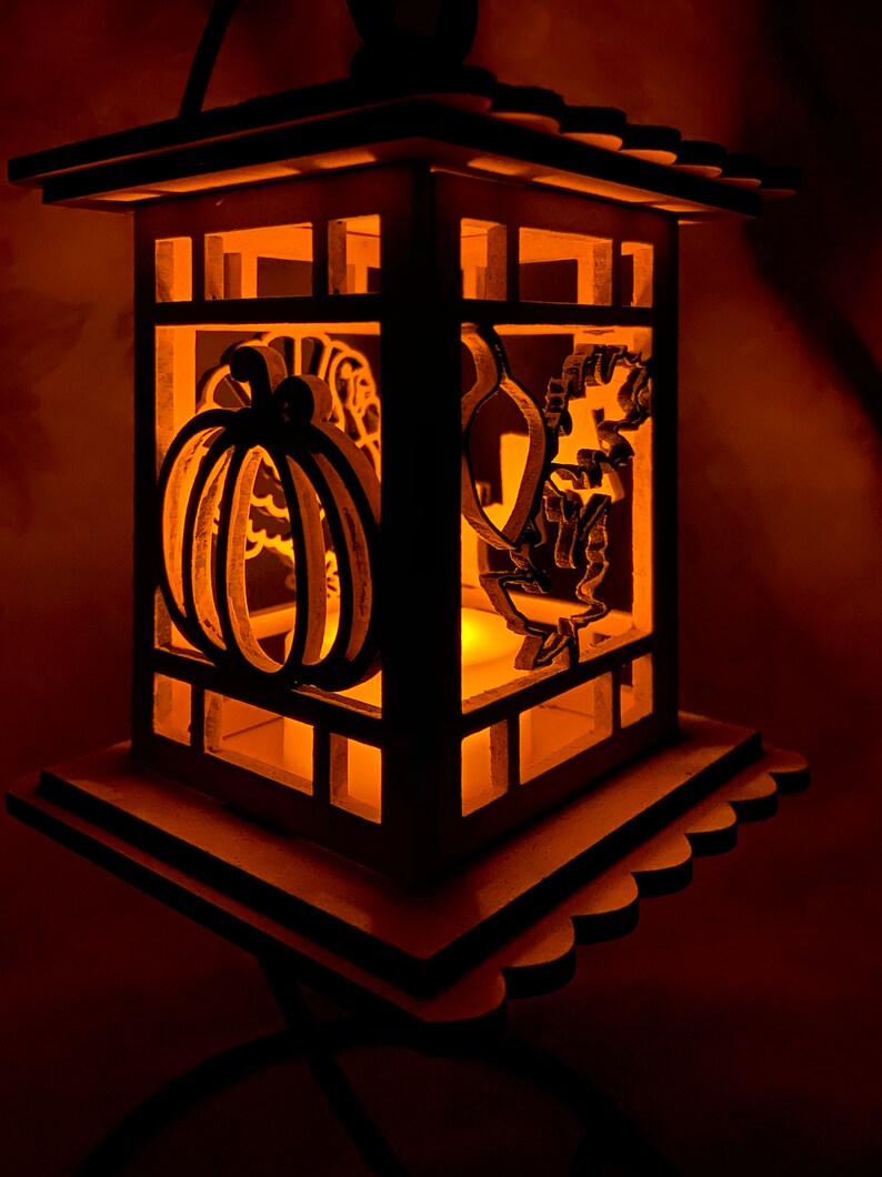 May include: A wooden lantern with a light inside, featuring a pumpkin and a turkey cut-out design. The lantern is lit and glows a warm orange color.