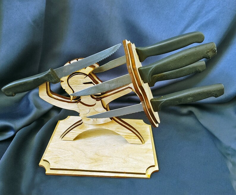 May include: Wooden knife holder shaped like a person holding multiple knives. The holder is made of light brown wood and the knives are black.