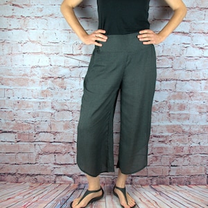 Puede incluir: Una persona con una camiseta negra de manga corta y unos pantalones culotte grises oscuros con un sutil estampado de puntos. Los pantalones culotte son de pernera ancha y llegan a la mitad de la pantorrilla. La persona tambi&eacute;n lleva sandalias negras. El fondo es una pared de ladrillo y un suelo de madera.