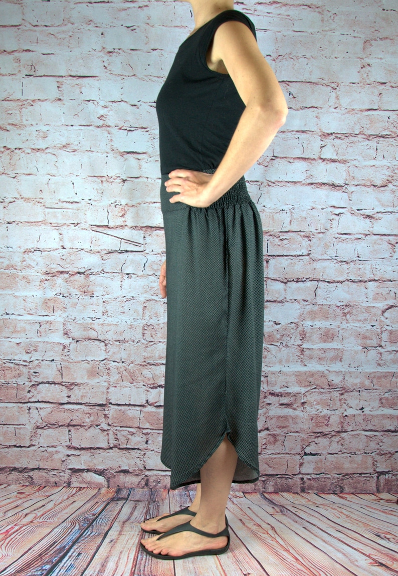 Puede incluir: Una camiseta sin mangas negra y una falda gris oscuro con un sutil estampado de puntos. La falda tiene una cintura el&aacute;stica y una abertura. La persona lleva sandalias negras.