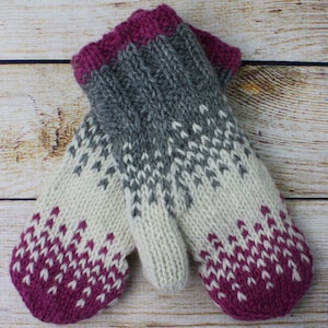 Könnte beinhalten: Ein Paar gestrickte Fäustlinge mit einem weißen, grauen und rosafarbenen Farbmuster. Die Fäustlinge haben ein traditionelles skandinavisches Design.