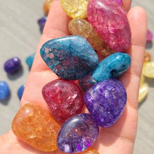 May include: A collection of tumbled chakra stones in various colors, including red, orange, yellow, green, blue, indigo, and violet. The stones are smooth and polished, with a natural, crystalline texture.