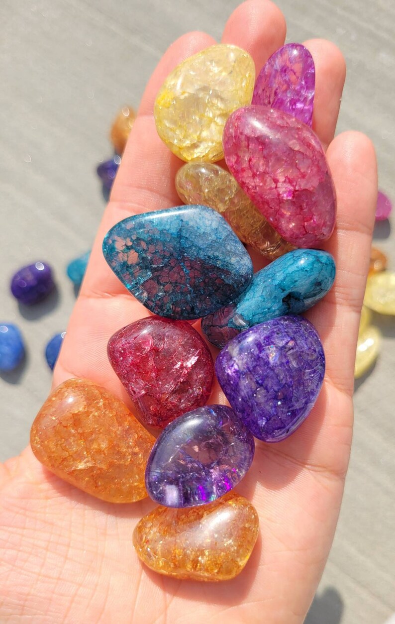 May include: A collection of tumbled chakra stones in various colors, including red, orange, yellow, green, blue, indigo, and violet. The stones are smooth and polished, with a natural, crystalline texture.