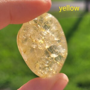 May include: A yellow, translucent, irregularly shaped stone with a textured surface. The stone is being held by a hand.
