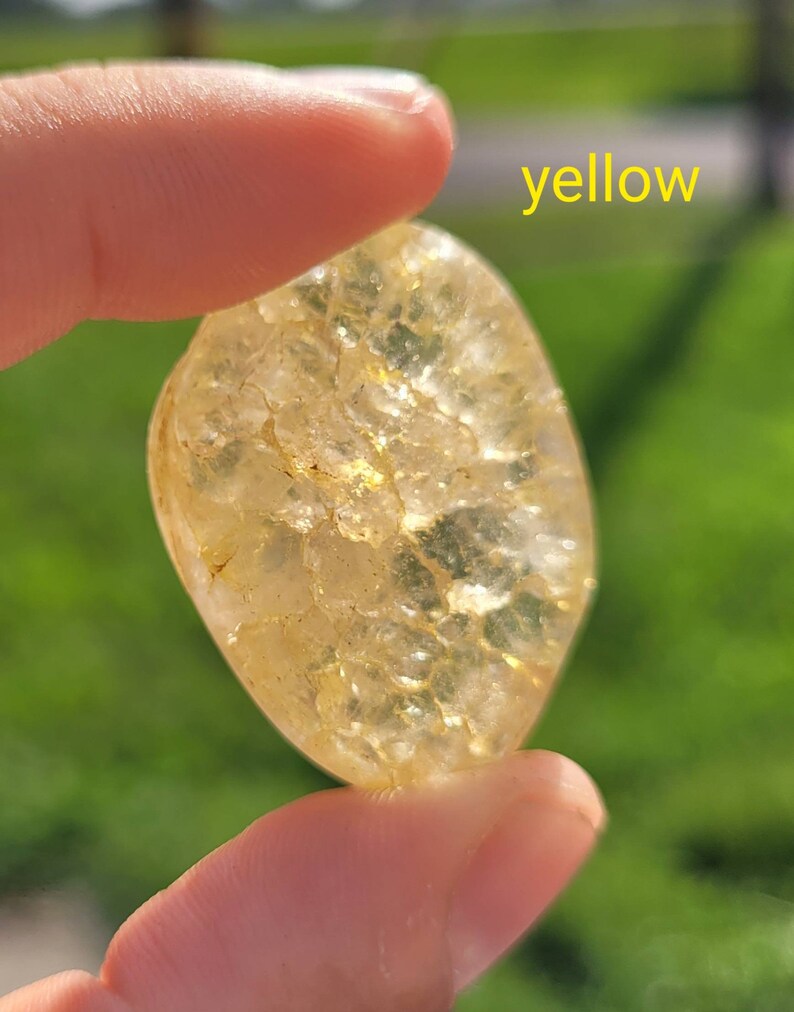 May include: A yellow, translucent, irregularly shaped stone with a textured surface. The stone is being held by a hand.