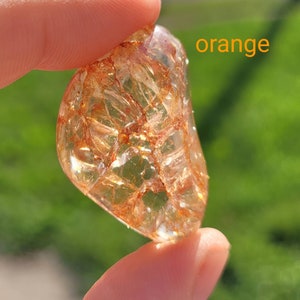 May include: A clear, orange, translucent stone with a unique, intricate pattern of inclusions. The stone is being held in a hand.