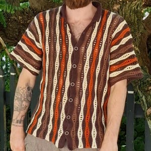 Puede incluir: Camisa de crochet de manga corta con botones y un patr&oacute;n de rayas verticales. La camisa presenta rayas alternas marrones, crema y naranjas. El cuello y la tapeta de botones son de color marr&oacute;n liso. Corte holgado.