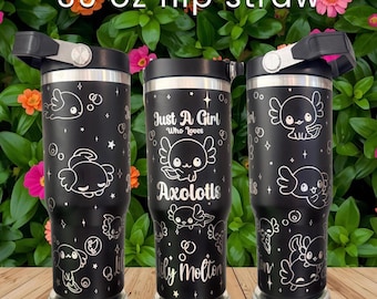 Puede incluir: Tres vasos negros de 30 oz con pajitas abatibles, con dibujos lineales blancos de ajolotes, estrellas y burbujas. El vaso central muestra el texto 'Just A Girl Who Loves Axolotls' y el nombre 'Lily Molton' en una fuente de color plateado.