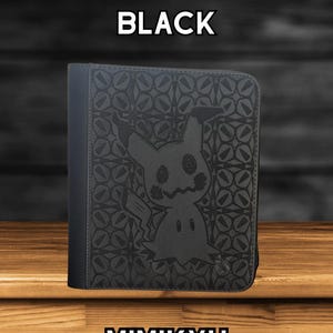 May include: Black 4-page top loader TCG binder with a Mimikyu design. The binder features a Mimikyu graphic and the word "Mimikyu" at the bottom. The text "4 PAGE TOP LOADER TCG BINDER BLACK" is at the top.