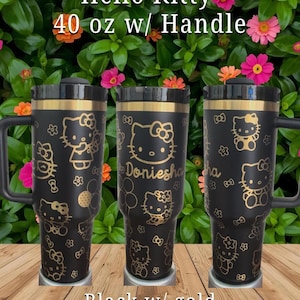 Puede incluir: Tres vasos negros de 1,18 litros con asa, con gráficos dorados de Hello Kitty y motivos florales. El vaso central muestra el nombre Doniesha en letra dorada. Cada vaso tiene una tapa negra y un borde superior de color dorado.