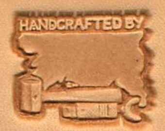 May include: A leather stamp with the text "HANDCRAFTED BY" and a blank space for a name. The stamp also features a hammer and a wrench.