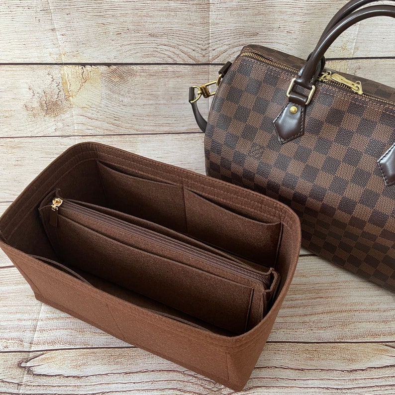 May include: Brown felt bag organizer with multiple pockets and a zippered compartment. The organizer is designed to fit inside a brown and tan checkered handbag.