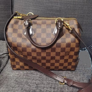 May include: A brown and tan checkered leather handbag with a gold zipper and a brown leather strap.