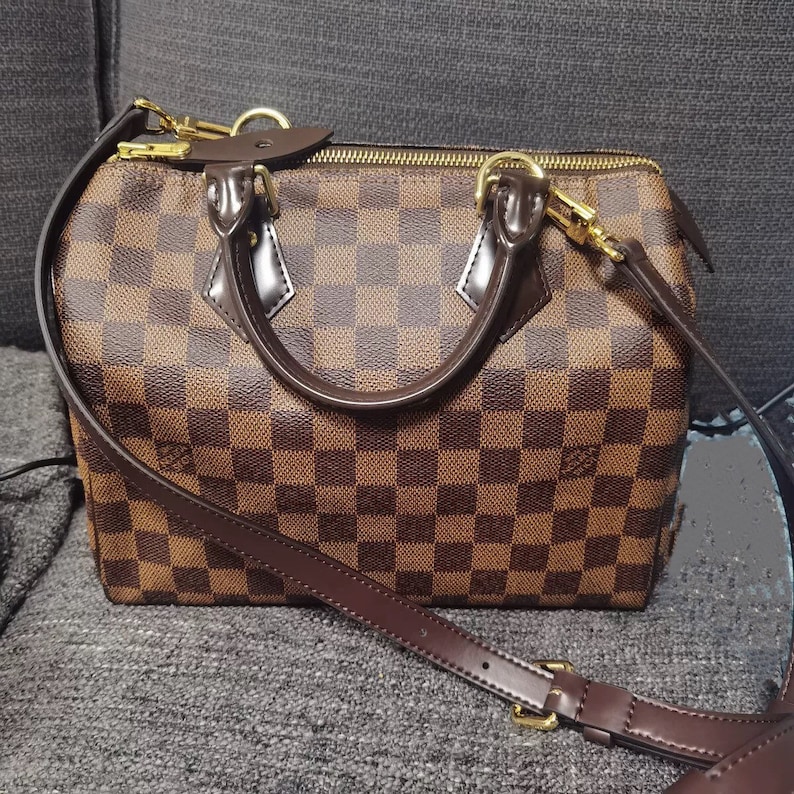 May include: A brown and tan checkered leather handbag with a gold zipper and a brown leather strap.