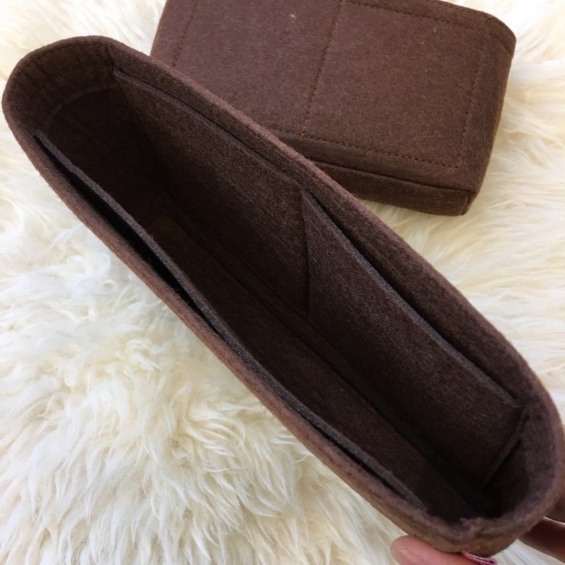 May include: Brown felt bag organiser with multiple compartments and pockets. The organiser is designed to fit inside a larger bag.