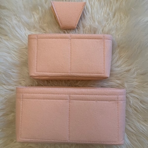 May include: A set of three pink felt bag organisers. The largest organiser has three compartments, the medium organiser has two compartments, and the smallest organiser is a triangular shape.