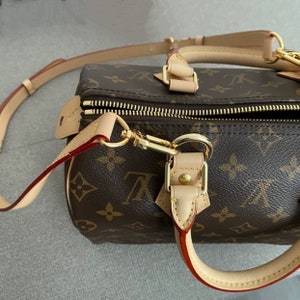 May include: A brown and tan leather handbag with a gold zipper and hardware. The bag has a monogram pattern and a long strap.