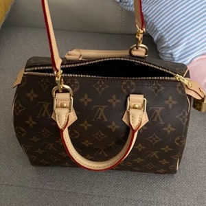 May include: A brown and tan leather handbag with a gold chain strap and a red leather trim. The bag has a monogram pattern and a gold zipper.