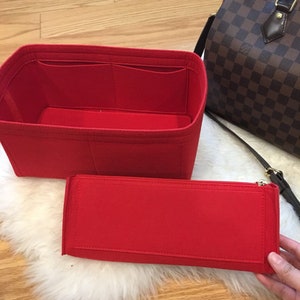 May include: Red felt bag organizer with multiple compartments and a separate zippered pouch. The organizer is designed to fit inside a larger bag.