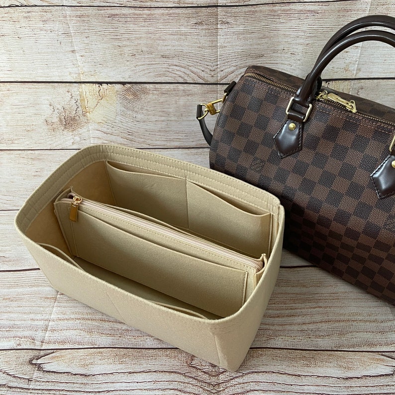 May include: Beige felt bag organizer with multiple pockets and a zippered compartment. The organizer is designed to fit inside a brown and tan checkered handbag.