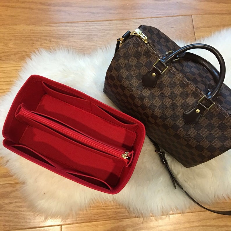 May include: Red felt bag organizer with multiple compartments and a zippered pocket. The organizer is designed to fit inside a brown and tan checkered handbag.