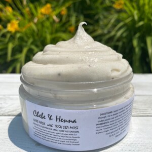 May include: A clear plastic jar filled with a thick, off-white hair mask featuring small dark specks. The white label reads Chebe & Henna Hair Mask with Irish Sea Moss, Growth Support & Moisture Retention, along with directions and ingredients.