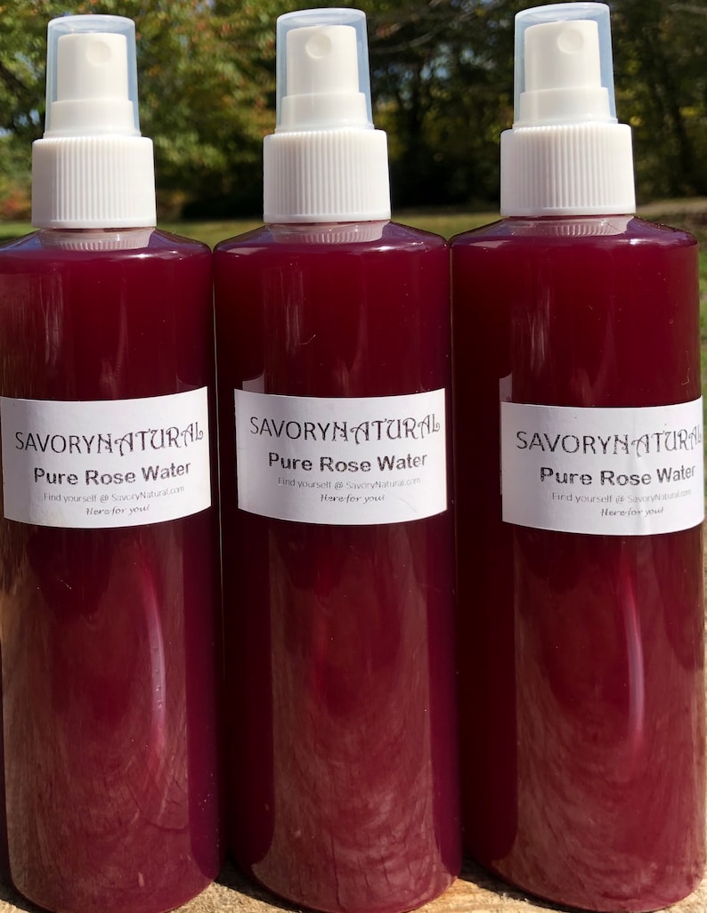 May include: Three glass bottles with white spray tops filled with a deep red liquid. Each bottle has a white label with the text "SAVORYNATURAL Pure Rose Water Find yourself @SavoryNatural.com Here for you!"