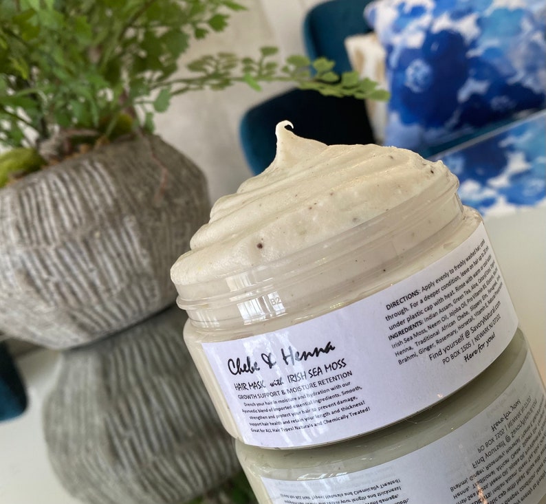 May include: A clear plastic jar filled with a thick, pale green hair mask featuring a swirled top. The white label reads Chebe & Henna Hair Mask with Irish Sea Moss, Growth Support & Moisture Retention, along with directions and ingredients.
