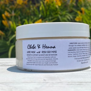 May include: A white plastic jar containing Chebe & Henna hair mask with Irish Sea Moss. The label features black text detailing growth support, moisture retention, directions, and ingredients, including Indian Assam, Green Tea, and Aloe Vera.