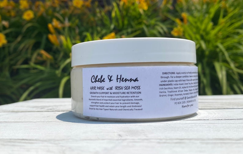 May include: A white plastic jar containing Chebe & Henna hair mask with Irish Sea Moss. The label features black text detailing growth support, moisture retention, directions, and ingredients, including Indian Assam, Green Tea, and Aloe Vera.
