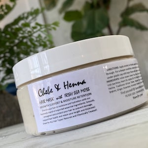 May include: A white plastic jar of Chebe & Henna hair mask with Irish Sea Moss. The label features black text detailing growth support, moisture retention, directions, and ingredients including Indian Assam, Green Tea, Aloe, and African Chebe.