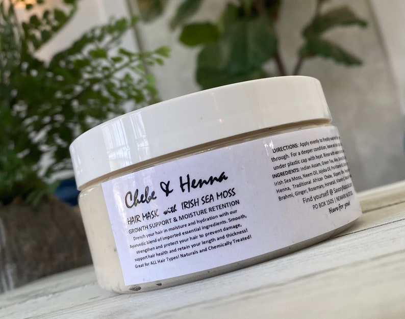 May include: A white plastic jar of Chebe & Henna hair mask with Irish Sea Moss. The label features black text detailing growth support, moisture retention, directions, and ingredients including Indian Assam, Green Tea, Aloe, and African Chebe.