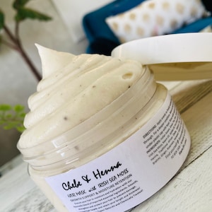 May include: A clear plastic jar filled with a thick, off-white hair mask featuring visible dark specks. The label reads Chebe & Henna Hair Mask with Irish Sea Moss, Growth Support & Moisture Retention, along with directions and ingredients list.