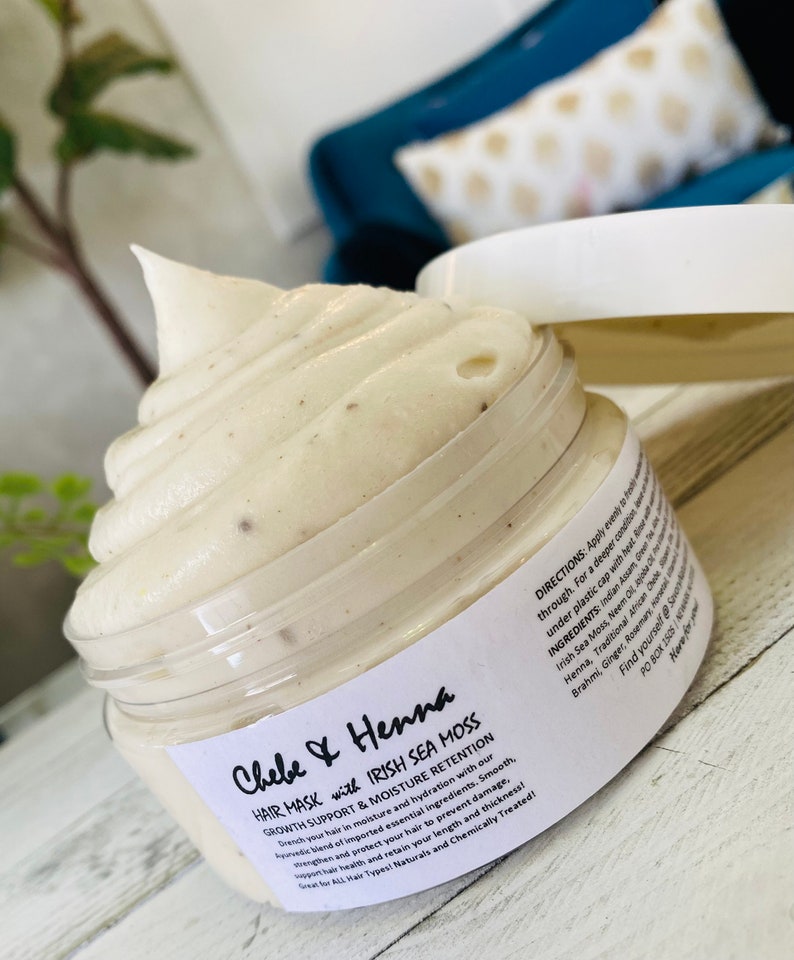 May include: A clear plastic jar filled with a thick, off-white hair mask featuring visible dark specks. The label reads Chebe & Henna Hair Mask with Irish Sea Moss, Growth Support & Moisture Retention, along with directions and ingredients list.