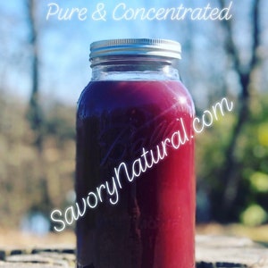 May include: A glass jar filled with a deep red liquid, labelled "Rose Water Pure & Concentrated" and "SavoryNatural.com". The jar has a silver lid and is sitting on a wooden surface. The jar is labelled with "64oz".