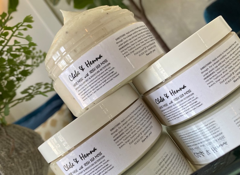 May include: Three clear plastic jars filled with a thick, off-white Chebe and Henna hair mask with Irish Sea Moss. Each jar features a white label with black text detailing directions, ingredients, and the product name in a script font.