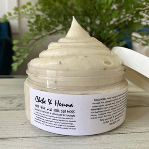 May include: A clear plastic jar filled with a thick, off-white hair mask cream topped with a swirl. The white label reads Chebe & Henna Hair Mask with Irish Sea Moss, Growth Support & Moisture Retention, along with directions, ingredients, and contact info.
