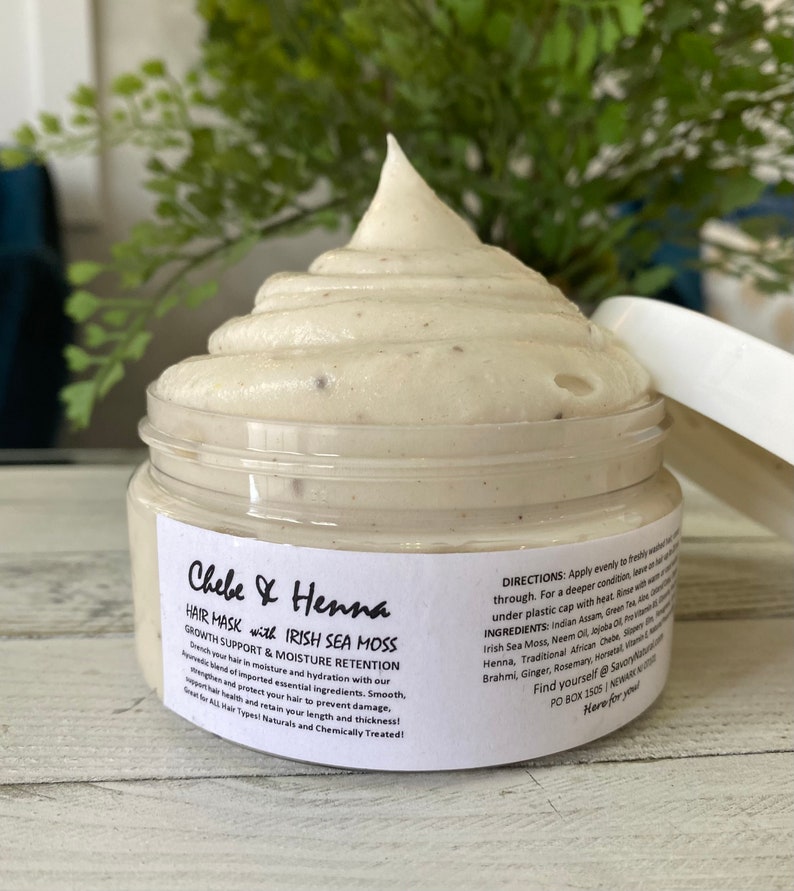 May include: A clear plastic jar filled with a thick, off-white hair mask cream topped with a swirl. The white label reads Chebe & Henna Hair Mask with Irish Sea Moss, Growth Support & Moisture Retention, along with directions, ingredients, and contact info.