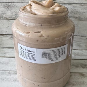 May include: A large clear plastic jar filled with a thick beige hair mask containing visible dark specks. The label reads Chebe & Henna Hair Mask with Irish Sea Moss, Growth Support & Moisture Retention, including directions, ingredients, and contact information.