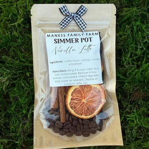 May include: A clear cellophane bag containing a simmer pot kit. The kit includes coffee beans, cinnamon sticks, and a dried orange slice. The bag is tied with a black and white checkered bow and includes a label that reads "Vanilla Latte."