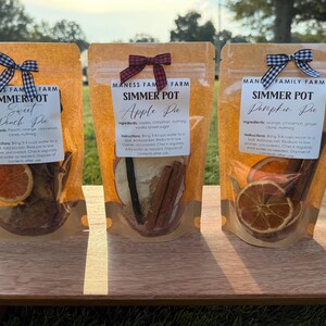 May include: Three clear bags of simmer pot ingredients, each with a different bow. The bags are labeled "Sweet Peach Pie", "Apple Pie", and "Pumpkin Pie". Each bag contains dried fruit and spices.