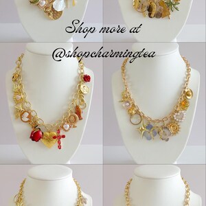 Peut inclure: Six colliers dor&eacute;s &agrave; breloques sur des bustes blancs. Chaque collier pr&eacute;sente divers charms, dont des coquillages, des croix, des c&oelig;urs et des &eacute;toiles. Le texte "Shop more at @shopcharmingtea" est visible.