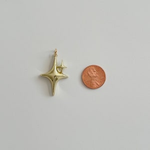 Peut inclure: Un pendentif en forme d'&eacute;toile dor&eacute;e avec une petite &eacute;toile attach&eacute;e. Le pendentif est brillant et r&eacute;fl&eacute;chissant. Une pi&egrave;ce de monnaie est &agrave; c&ocirc;t&eacute; du pendentif pour la comparaison de taille. Le pendentif est probablement pour les bijoux.