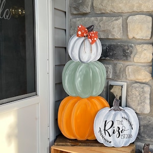 May include: A stacked pumpkin decoration with three pumpkins in white, green, and orange. The top pumpkin has a red and white polka dot bow. A separate white pumpkin with the text "The Rizo EST. 2006" is also present.