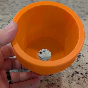 May include: Orange plastic mold with a circular opening in the center. The mold is designed for creating a round object.