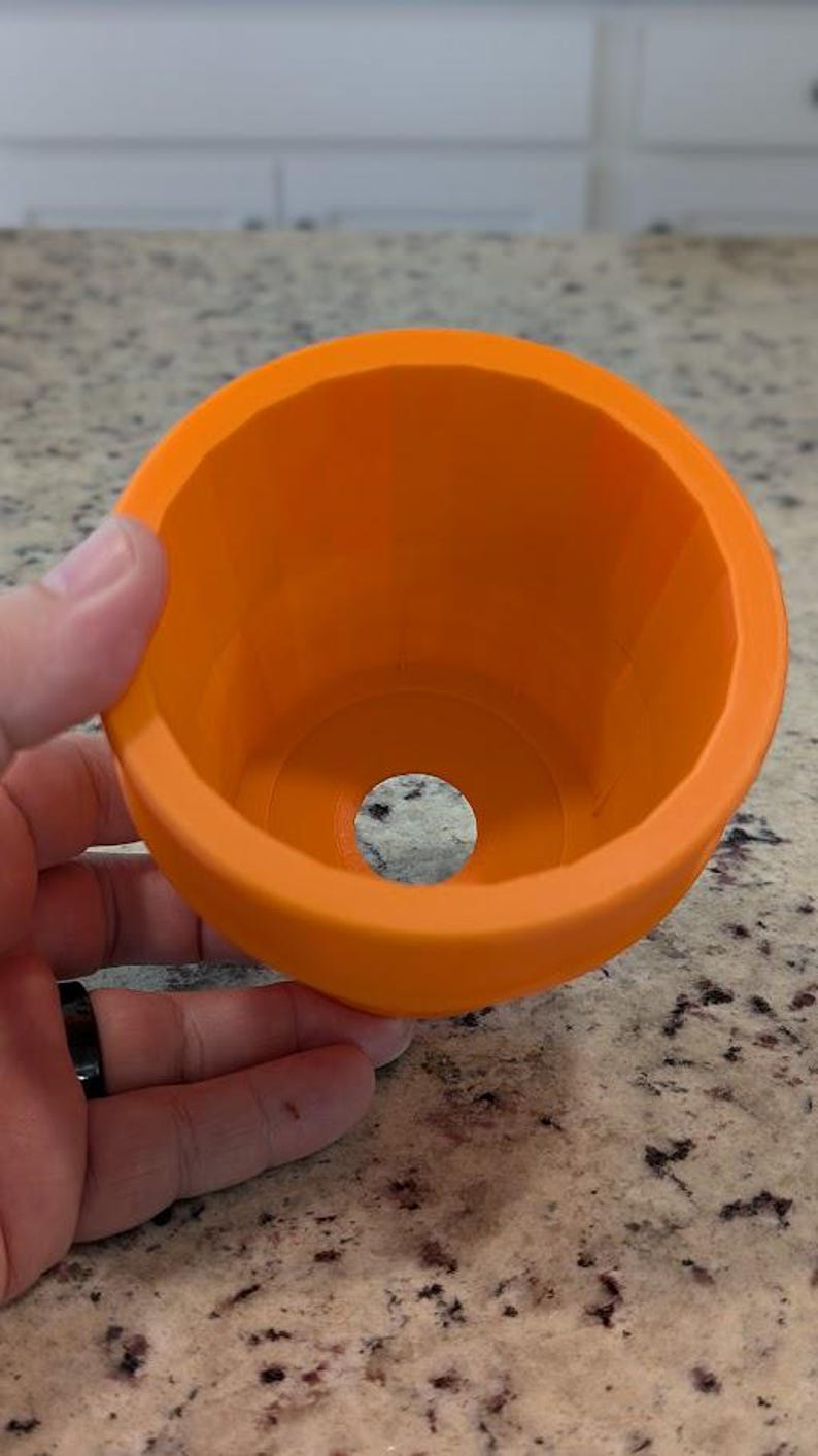 May include: Orange plastic mold with a circular opening in the center. The mold is designed for creating a round object.