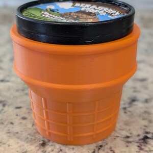 May include: Orange plastic ice cream container with a black lid. The lid has a Ben & Jerry's logo with a cartoon character and the words "Cookie Dough".