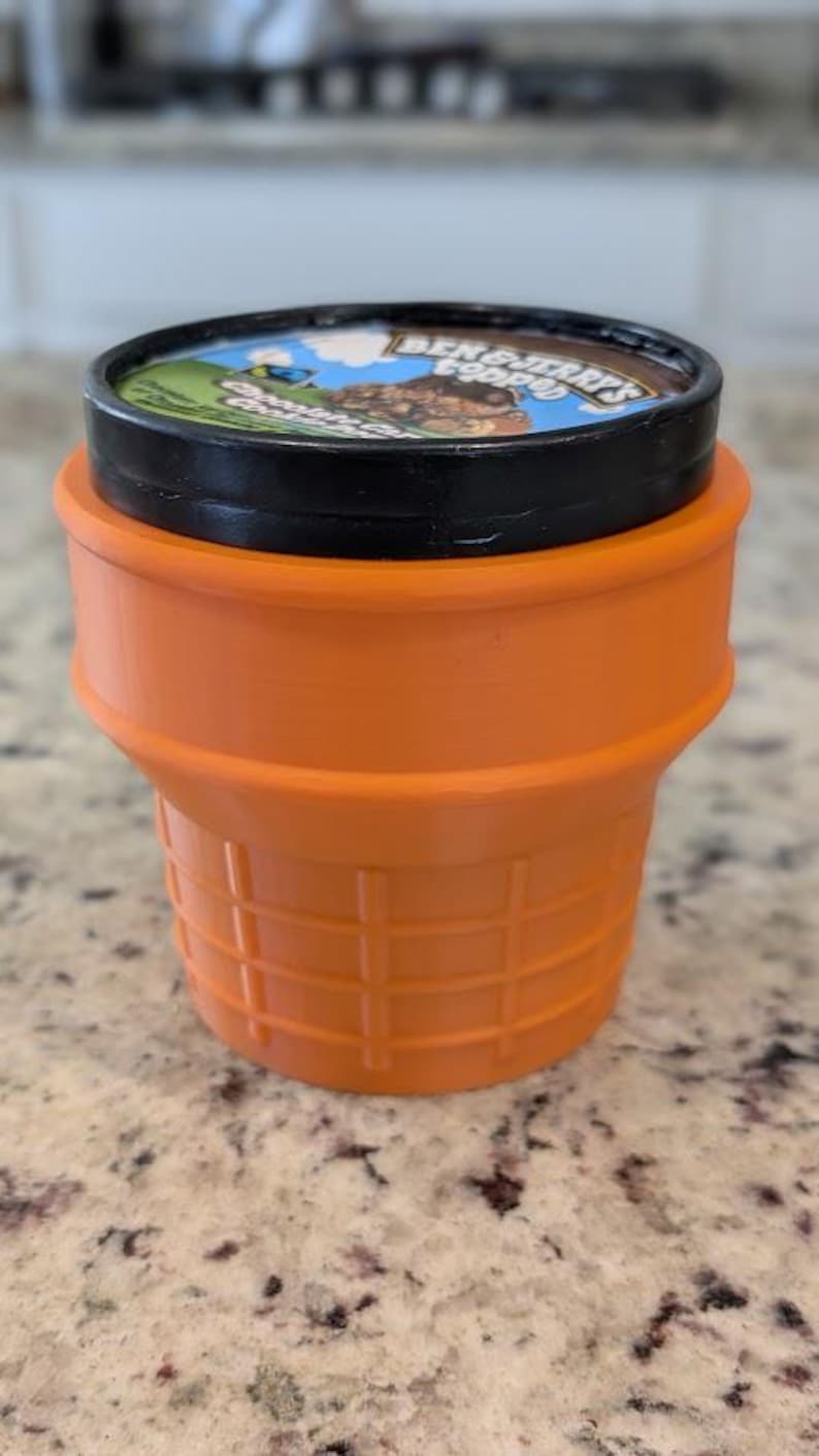 May include: Orange plastic ice cream container with a black lid. The lid has a Ben & Jerry's logo with a cartoon character and the words "Cookie Dough".